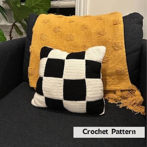 May include: A black and white checkered crochet cushion on a black armchair with a yellow throw blanket. The throw blanket has a textured, bumpy surface. The text "Crochet Pattern" is visible at the bottom of the image.
