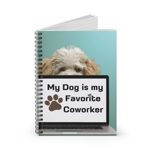 May include: A spiral bound notebook with a light blue background featuring a white laptop with the text "My Dog is my Favorite Coworker" and a brown paw print. A fluffy white and brown dog is peeking over the top of the laptop screen.