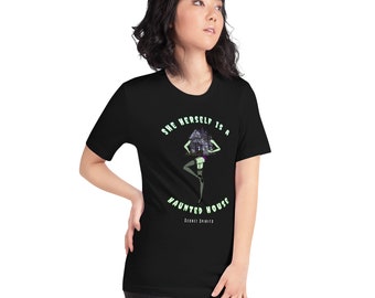 May include: Black t-shirt featuring a green and black illustration of a woman with a house on her head. The text "She herself is a haunted house" is printed on the shirt.