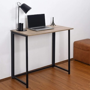 May include: A small, foldable desk with a light wood top and black metal legs. A laptop, lamp, and decorative Eiffel Tower are on the desk.