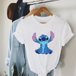 May include: White t-shirt with a blue Stitch character from the Disney movie Lilo & Stitch. Stitch is sitting with his arms crossed and has a big smile on his face.