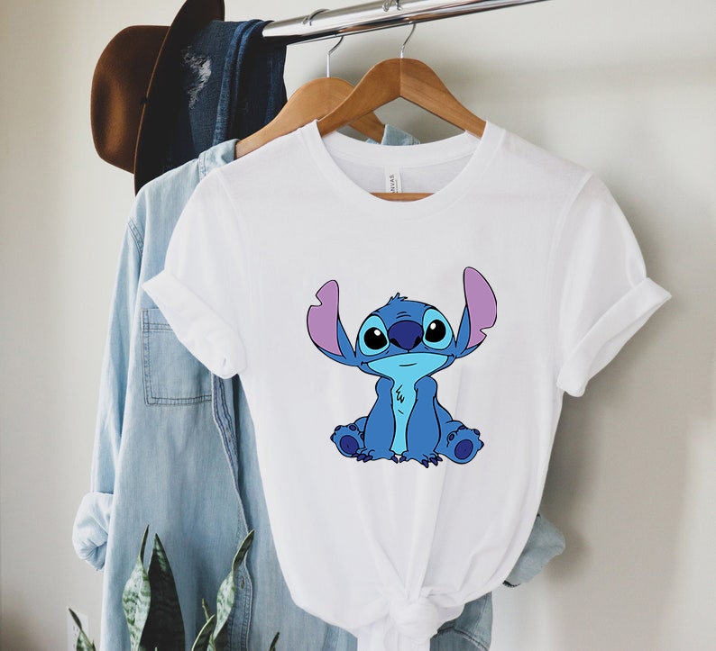May include: White t-shirt with a blue Stitch character from the Disney movie Lilo & Stitch. Stitch is sitting with his arms crossed and has a big smile on his face.