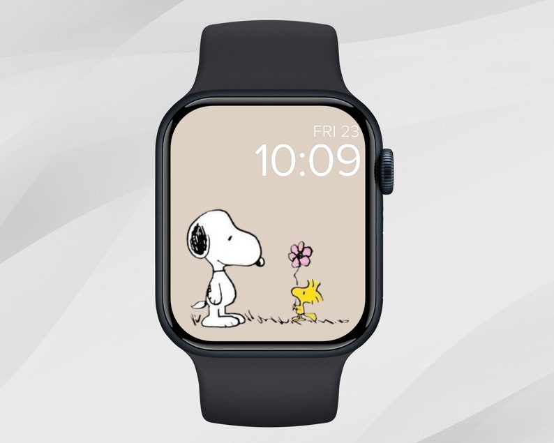 May include: A black Apple Watch with a white watch face displaying the time 10:09 and the date FRI 23. The watch face features a cartoon image of Snoopy holding a pink flower and Woodstock standing next to him.