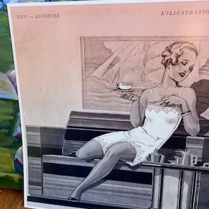 May include: Vintage black and white print of a woman in a white slip holding a teacup. The print has the text "XXIV - ANNONCES" and "L'ILLUSTRATION". The woman is seated on a striped sofa, with a table holding a tea set.