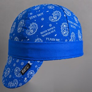 May include: A bright blue welding cap featuring a white paisley pattern and text that reads STAY HOT, HOOD DOWN WORLD OUT, and BURN BABY BURN. The cap has a solid blue band and a small black tag on the brim with the white text VELOCAPS printed on it.