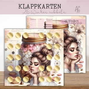 Könnte beinhalten: Zwei Karten mit einem Glas-Design und einem Frauenporträt. Die Karten haben goldene Rubbelkreise. Der Text oben lautet "KLAPPKARTEN" und "26 Wochen rubbeln". Der Hintergrund ist im weichen Aquarellstil mit floralen Elementen.