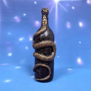 May include: A black glass bottle with a gold snake wrapped around it. The snake is sculpted and has a textured surface.