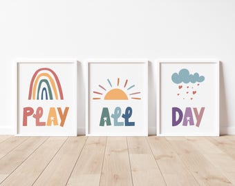 May include: Three white framed prints with colorful illustrations and text. The first print features a rainbow with the word "PLAY" underneath. The second print features a sun with the word "ALL" underneath. The third print features a cloud with raindrops and the word "DAY" underneath.