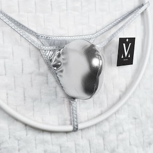 May include: Silver thong underwear with a pouch. The thong is made of a shiny, metallic material. A black tag with a white "V" logo is attached.
