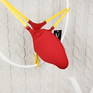 May include: Red and yellow lingerie suspended on a white circular frame. The lingerie features a red, teardrop-shaped front panel and yellow straps. A small tag with a black and white logo is attached.