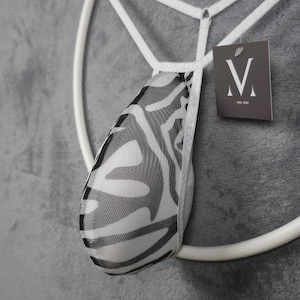 May include: A white and black zebra print thong with a white elastic waistband. The thong is hanging from a white circular frame. A tag with the letter "V" is attached.