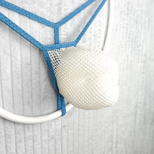 Könnte beinhalten: Ein blauer Tanga mit einer weißen Netztasche. Das Kleidungsstück besteht aus dünnen, elastischen blauen Riemen, die ein geometrisches Muster bilden und mit einem strukturierten, halbtransparenten weißen Netzstoff verbunden sind.