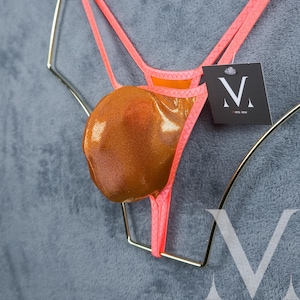 May include: A pink and gold thong with a shiny gold pouch. The thong is hanging on a gold hanger. The tag on the thong reads "V - 100% SILK"