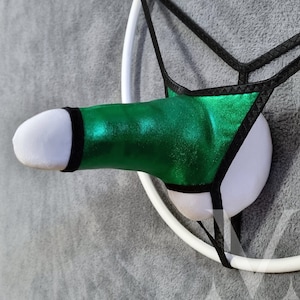 May include: A novelty item featuring a white, plush phallus with a metallic green sheath and black trim. The design includes a black thong-style support and a white ring. The item is displayed against a gray background.