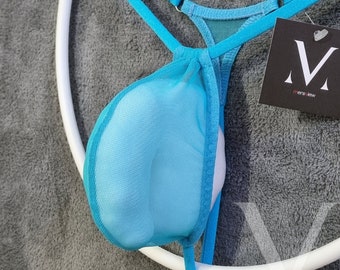 Op de afbeelding: Een turquoise mesh string met een witte binnenkant, opgehangen aan een wit cirkelvormig frame. De string heeft dunne bandjes en een klein label met de merknaam "mens jew" in een zwart-wit ontwerp.