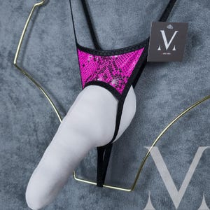 May include: Black and pink lingerie with a snake print design. The lingerie has a strap that goes around the waist and a strap that goes around the neck. The lingerie is hanging on a hanger.