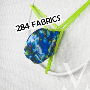 Può includere: Un perizoma con una tasca dal motivo astratto marmorizzato blu, verde e bianco e cinturini elastici verde lime brillante. Il testo 284 FABRICS è stampato in nero sopra la tasca. Il capo è esposto su una cornice circolare bianca.