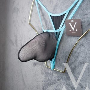 May include: Black and blue lingerie with a mesh pouch and a tag with the letter "V" on it. The lingerie is hanging on a gold-colored metal frame against a gray background. The lingerie has a unique design.