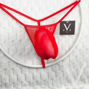 May include: Red lingerie set with a thong design and a tulip-shaped detail. The set is made of sheer fabric and includes a tag with a stylized "V" logo. The lingerie is displayed against a white background.