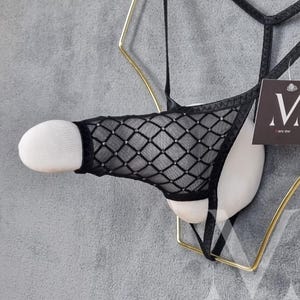 Könnte beinhalten: Schwarze Netz-Dessous mit Rautenmuster und weißem Besatz. Die Dessous sind an einem Kleiderbügel aufgehängt.