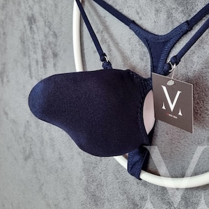 Könnte beinhalten: Ein marineblauer BH mit zarten Trägern und einem passenden String-Tanga. Der BH hat ein glattes, nahtloses Design. Ein Etikett mit dem Buchstaben "V" ist am BH befestigt.