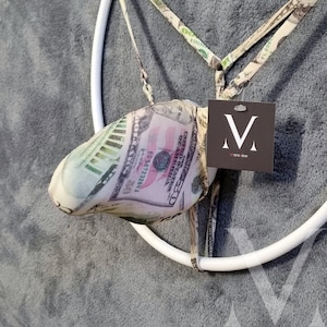 Könnte beinhalten: Ein neuartiges Kleidungsstück mit Gelddruckdesign, das in einem weißen kreisförmigen Rahmen aufgehängt ist. Das Kleidungsstück hat ein Etikett mit dem Markennamen "mensview".