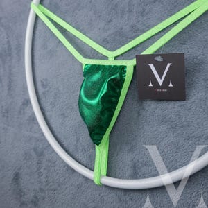 Op de afbeelding: Groene en limoengroene string onderbroek met een glanzende afwerking. De onderbroek heeft een klein label met de letter "M" en de tekst "mens low" erop.