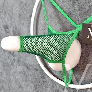 May include: Green mesh underwear with a white fabric insert. The underwear is suspended by a white circular frame. The design features a net-like pattern and a vibrant green color.