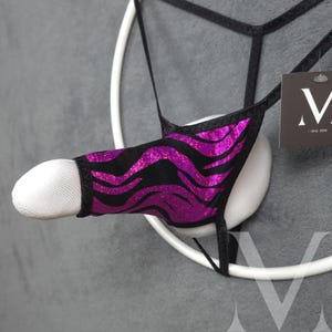 May include: A black and purple zebra-striped thong-style garment. The garment is displayed on a white form, with a tag that reads "mens jew". The background is a solid gray.