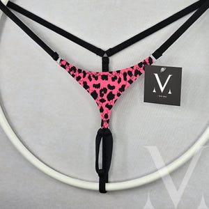 Op de afbeelding: Roze en zwart luipaardprint lingerie met een zwarte verstelbare band en een zwarte ring in het midden.