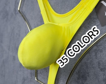 Op de afbeelding: Felgeel string-ondergoed met een pouch-ontwerp. Het kledingstuk wordt gepresenteerd op een goudkleurige hanger tegen een grijze achtergrond. De tekst "35 COLORS" is zichtbaar op de afbeelding.