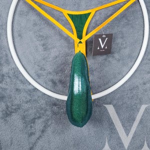May include: A green and yellow jockstrap with a sparkly green pouch. The jockstrap is hanging on a white ring. The tag says "M" with a crown above the letter.