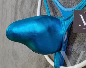 Op de afbeelding: Een turquoise metallic string badpak met een wit ringdetail. Het badpak heeft een zakachtige voorkant en dunne bandjes. Een zwart label met een wit "M"-logo is bevestigd.