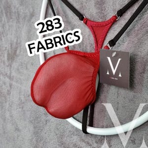 Op de afbeelding: Rode lingerie met zwarte bandjes en een label met de tekst "mens-lew". De lingerie hangt aan een witte ronde hanger. De tekst "283 FABRICS" staat in een wit kader linksboven.
