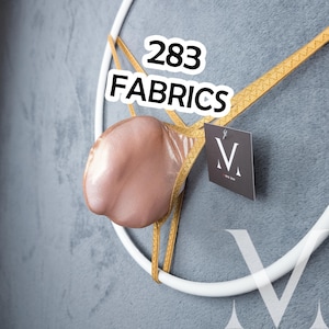 Pode incluir: Uma tanga cor de pele com acabamento dourado está suspensa em uma moldura circular branca. O texto "283 FABRICS" é exibido acima da tanga. Uma pequena etiqueta com a letra "V" está anexada.