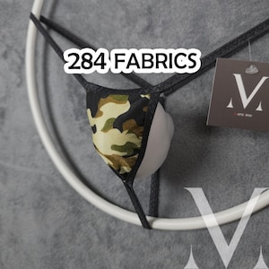 Peut inclure: Un string avec un motif camouflage dans des tons de vert, marron et noir avec de fines bretelles élastiques noires. Le texte 284 FABRICS est visible en haut, et une étiquette marron foncé avec un logo M blanc est attachée sur le côté.