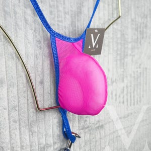 May include: A bright pink thong with a blue trim and straps. The thong is made of a mesh material and has a small tag with a stylized "V" logo. The garment is hanging on a gold-colored metal hanger.