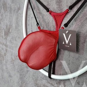 Può includere: Completo di lingerie rosso con un davanti trasparente a forma di petalo e sottili spalline nere. Il set include un'etichetta con un logo "M" stilizzato e il testo "mens-lew". La lingerie è esposta su un appendiabiti circolare bianco.