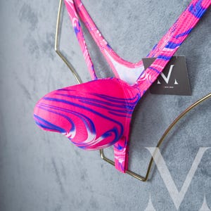 Op de afbeelding: Een felroze en blauw patroon string badpak. Het badpak heeft een kenmerkend wervelend patroon in roze, blauw en wit. De bandjes zijn dun en delicaat en de algehele stijl is modern en opvallend.