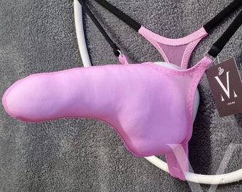May include: A light pink thong-style undergarment with a pouch, suspended on a white circular hanger. The garment features black straps and a small tag with a logo. The fabric appears to be a soft, breathable material.