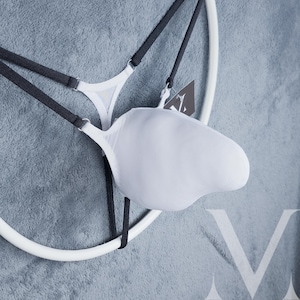 May include: White lingerie set with black straps and a unique design. The set is displayed on a white circular hanger against a gray background. A tag is attached to the lingerie.