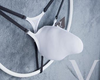 May include: White lingerie set with black straps and a unique design. The set is displayed on a white circular hanger against a gray background. A tag is attached to the lingerie.