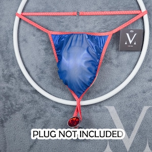 May include: A blue satin jockstrap with a red trim and a red ring attached to the bottom. The text "PLUG NOT INCLUDED" is printed below the jockstrap.