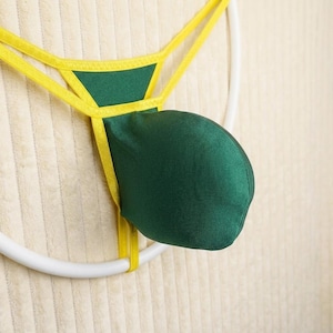 Könnte beinhalten: Ein Tanga mit einer dunkelgrünen Tasche und dünnen gelben elastischen Riemen. Das Kleidungsstück ist mit einem dreieckigen grünen Stoffeinsatz an der Vorderseite der Taille konstruiert, der mit einer abgerundeten, hervorstehenden grünen Tasche verbunden ist.