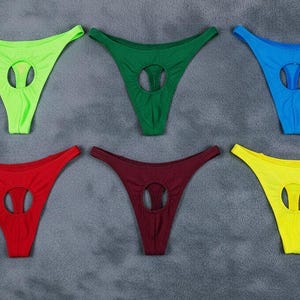 Könnte beinhalten: Sechs farbenfrohe String-Tangas in Grün, Rot, Blau, Gelb und Burgunderrot. Jeder hat einen kreisförmigen Ausschnitt. Die Kleidungsstücke werden auf einer grauen Oberfläche präsentiert.