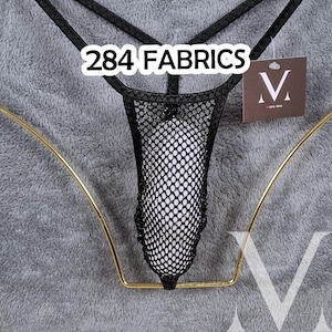 Op de afbeelding: Een zwarte visnet string met dunne bandjes en een centraal mesh paneel. Een bruin label met de letter V en de tekst 284 FABRICS is bevestigd. Het kledingstuk wordt gepresenteerd op een goudkleurig draadframe tegen een grijze achtergrond.
