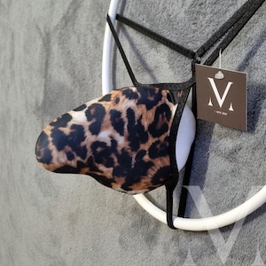 Op de afbeelding: Een zwarte en bruine string met luipaardprint met zwarte bandjes en een wit label met de tekst "VETE VYN" met een hoofdletter "V" in het midden.