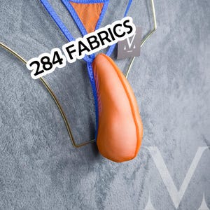 Può includere: Un perizoma con una tasca in rete arancione brillante e bordi blu, esposto su una gruccia in filo metallico dorato. Il testo 284 FABRICS è sovrapposto in bianco. Il capo include una piccola etichetta quadrata con un logo M bianco.
