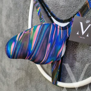 Könnte beinhalten: Ein schwarzer und irisierender blauer, rosa und grüner Jockstrap mit einem weißen elastischen Band und einem schwarzen Etikett mit der Aufschrift "menswear" in weißen Buchstaben.