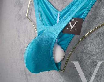 Op de afbeelding: Een turquoise blauwe zwembroek met een zak aan de voorkant. De zwembroek hangt aan een gouden hanger. Het label op de zwembroek zegt "M" voor "Menswear".